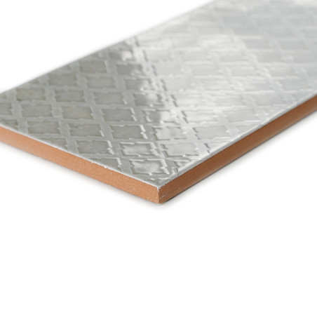 Un carreau rectangulaire affiche un motif géométrique brillant en relief, réfléchissant la lumière. Il repose sur une surface pl Un carreau rectangulaire affiche un motif géométrique brillant en relief, réfléchissant la lumière. Il repose sur une surface pl