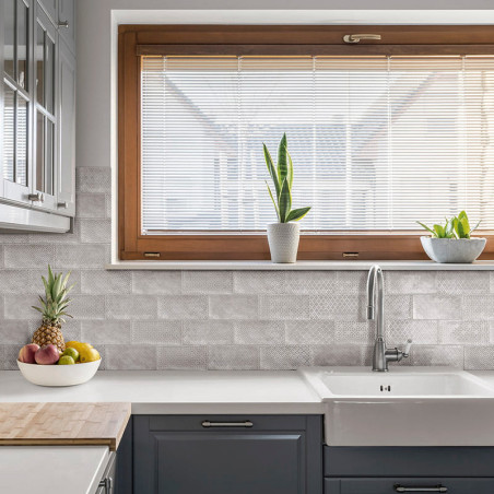 Een aanrecht bevindt zich onder een groot raam met zonwering. op een toonbank staan ​​een fruitschaal en potplanten, omgeven doo