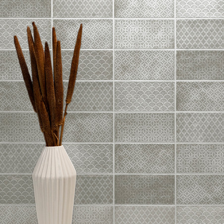 Een witte keramische vaas bevat hoge, bruine lisdodden. Daarachter bevindt zich een betegelde muur met een zich herhalend patroo