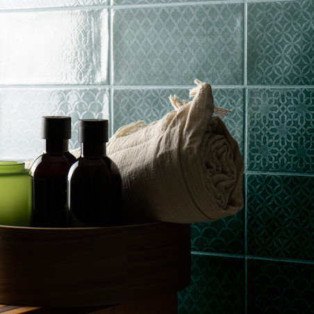 Mur carrelé avec des motifs géométriques complexes. Le premier plan montre un récipient rond en bois contenant des bouteilles so Mur carrelé avec des motifs géométriques complexes. Le premier plan montre un récipient rond en bois contenant des bouteilles so