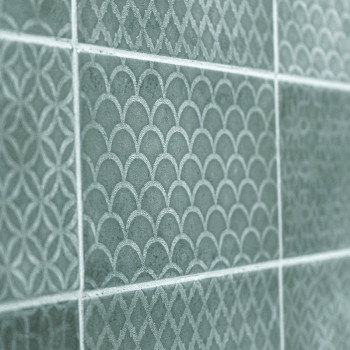Los azulejos de cerámica verde muestran patrones intrincados y repetidos de arcos y diamantes, creando una superficie de pared d