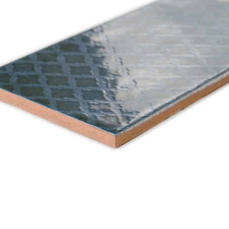 Un carreau de céramique rectangulaire présente une surface bleu foncé brillante avec un motif géométrique subtil, placé sur un f