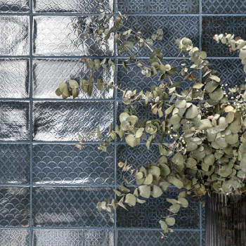 Des branches d'eucalyptus vertes s'étendent sur des carreaux de verre présentant des motifs géométriques en relief, créant un co