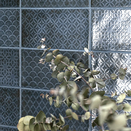 Les carreaux de céramique affichent des motifs géométriques complexes et variés dans un ton bleuâtre sourd. Les branches d'eucal