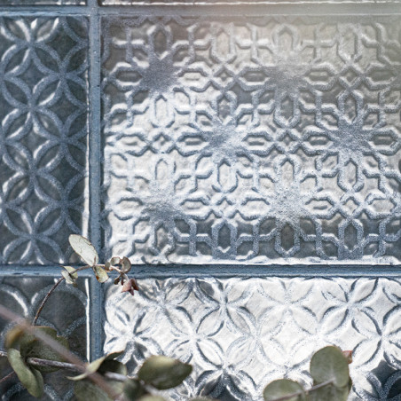Ladrilhos de vidro decorativos exibem padrões geométricos intrincados, refletindo a luz. Um raminho de pequenas folhas verdes re Ladrilhos de vidro decorativos exibem padrões geométricos intrincados, refletindo a luz. Um raminho de pequenas folhas verdes re