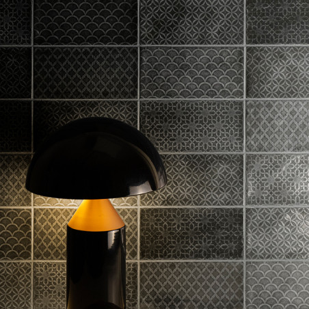 Uma lâmpada preta ilumina suavemente azulejos cinza intrincados com padrões geométricos e recortados em uma sala mal iluminada. Uma lâmpada preta ilumina suavemente azulejos cinza intrincados com padrões geométricos e recortados em uma sala mal iluminada.