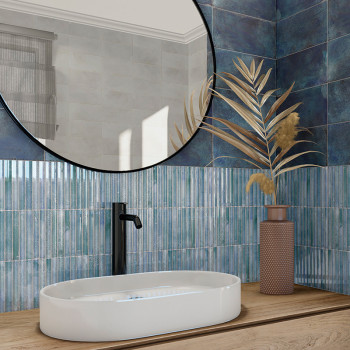 Un évier ovale blanc repose sur un comptoir en bois avec un robinet noir. Un grand miroir rond reflète des carreaux bleus textur