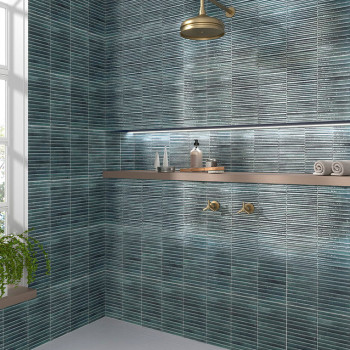 Rectangular blue-green tiles cover the walls, surrounding a modern bathroom with a brass showerhead, wooden shelf holding toilet