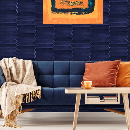Un mur carrelé bleu foncé présente une peinture abstraite orange. Un canapé bleu avec des oreillers et une couverture se trouve 