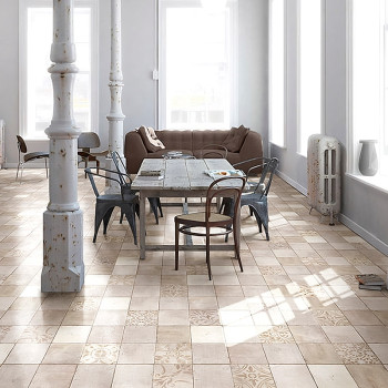 Een eettafel met gemengde stoelen staat op beige tegels met patronen, omgeven door vintage zuilen en natuurlijk licht in een rui