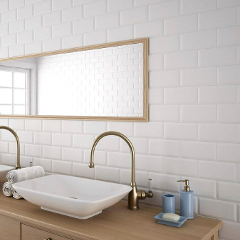 Witte rechthoekige tegels creëren een strakke achtergrond in een badkamer, met een spiegel met houten frame, dubbele koperen kra