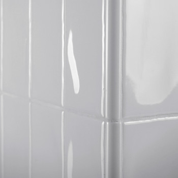 Des carreaux rectangulaires blancs brillants recouvrent un mur d’angle, réfléchissant la lumière selon un motif de grille lisse 