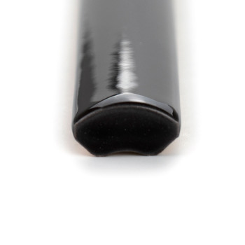 Un carreau de céramique quart de rond, noir et brillant, au bord lisse et incurvé, repose sur un fond uni et blanc, réfléchissan