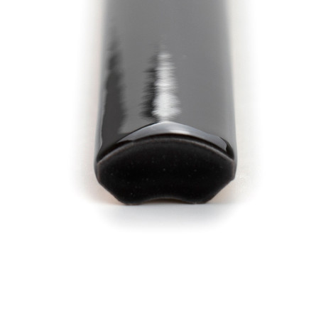 Eine glänzende, schwarze, viertelrunde Keramikfliese mit einer glatten, geschwungenen Kante ruht auf einem schlichten, weißen Hi Eine glänzende, schwarze, viertelrunde Keramikfliese mit einer glatten, geschwungenen Kante ruht auf einem schlichten, weißen Hi