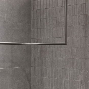 Gray rectangular tiles line a wall and floor corner, creating a modern, minimalist look. A metal frame intersects the tiles, add