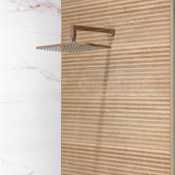 Une pomme de douche carrée en métal s'étend d'un mur, contre du bois à rayures verticales et des carreaux de marbre blanc adjace