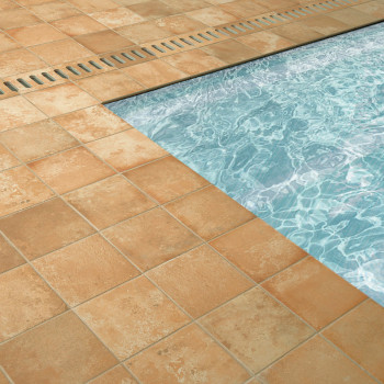 azulejos de terracota rodean una piscina azul brillante, con patrones de agua visibles. Una rejilla de metal se encuentra al lad