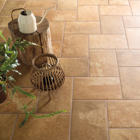 Un sol en carreaux de céramique rustique beige est disposé selon un motif à chevrons. Une théière blanche et une lanterne repose