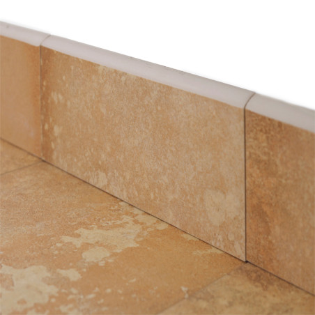 Les plinthes en céramique beige se trouvent à la base d'un mur, légèrement texturées, entourées de lignes de coulis et de plinthes adjacentes, indiquant une configuration de sol.