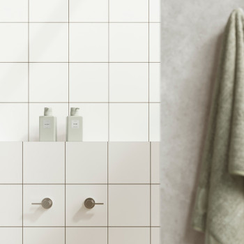 Los azulejos blancos forman una pared de baño con dos manijas cilíndricas debajo de dos botellas con las etiquetas `PELO` y `CUE