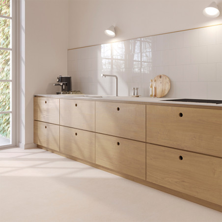 Una cocina moderna cuenta con gabinetes de madera clara contra paredes de azulejos blancos. Sobre el mostrador hay una cafetera 