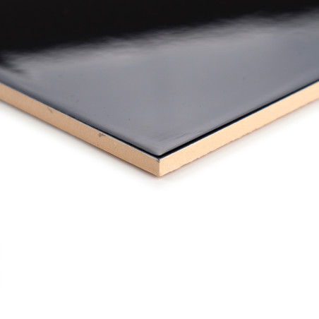 Un azulejo negro brillante con bordes beige descansa sobre un fondo blanco, mostrando su superficie lisa y sus esquinas limpias 