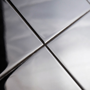 Vier glanzende, metalen tegels zijn uitgelijnd in een raster en reflecteren licht en schaduwen. Ze vormen elkaar kruisende lijne