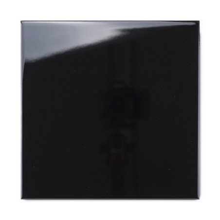 Un azulejo negro brillante refleja la luz, creando una superficie brillante y un reflejo de sombras, ambientado en un fondo vací