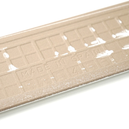 Strukturierte beige rechteckige Sockelleisten zeigen den erhabenen Text „MADE IN SPAIN“ zwischen schwachen weißen Markierungen vor einem schlichten weißen Hintergrund.