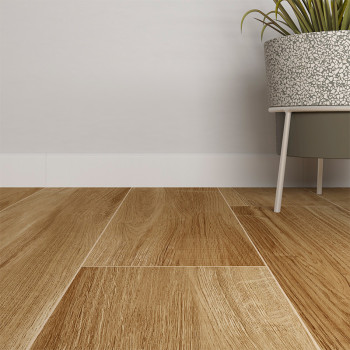 Rodapies de madera dispuestas cuidadosamente, asemejándose a tablas de roble natural. junto a ellos, una maceta gris con patas sostiene una planta verde, apoyada contra una pared blanca y lisa.