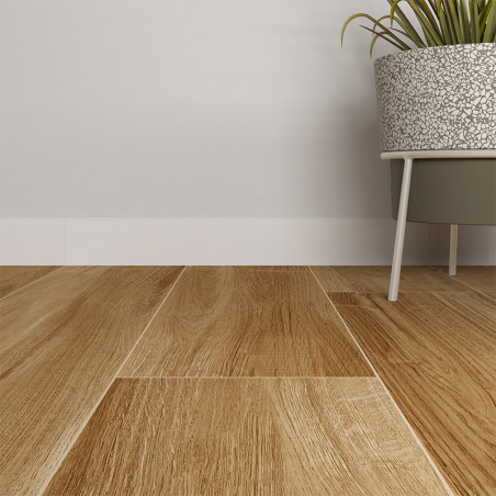 Rodapies de madera dispuestas cuidadosamente, asemejándose a tablas de roble natural. junto a ellos, una maceta gris con patas sostiene una planta verde, apoyada contra una pared blanca y lisa.