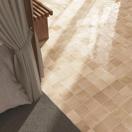 Glossy beige square tiles are laid on a sunlit floor, bordered by a gray carpet, next to a partially open curtain.