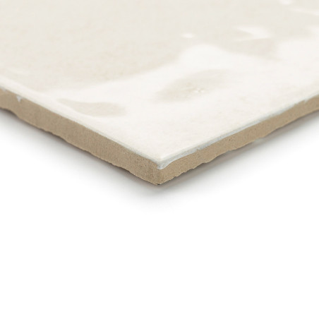 Un carreau de céramique repose à plat, affichant une surface brillante, lisse et de couleur crème avec des variations subtiles, 