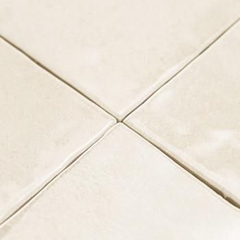 Carreaux de céramique de couleur crème disposés selon un motif en grille, avec une légère texture et des lignes de coulis visibl