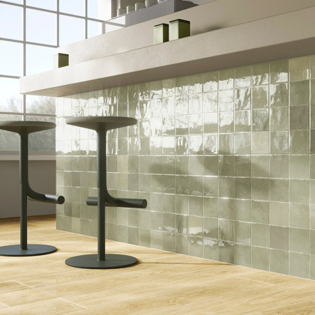 Glänzend grüne quadratische Fliesen reflektieren das Sonnenlicht und bedecken eine Küchenwand. Zwei moderne Barhocker stehen auf Glänzend grüne quadratische Fliesen reflektieren das Sonnenlicht und bedecken eine Küchenwand. Zwei moderne Barhocker stehen auf