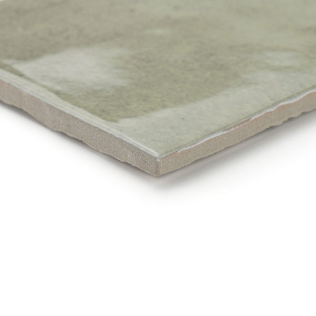 Un carreau rectangulaire présente une surface lisse, brillante et verdâtre avec des bords légèrement inégaux, reposant sur un fo