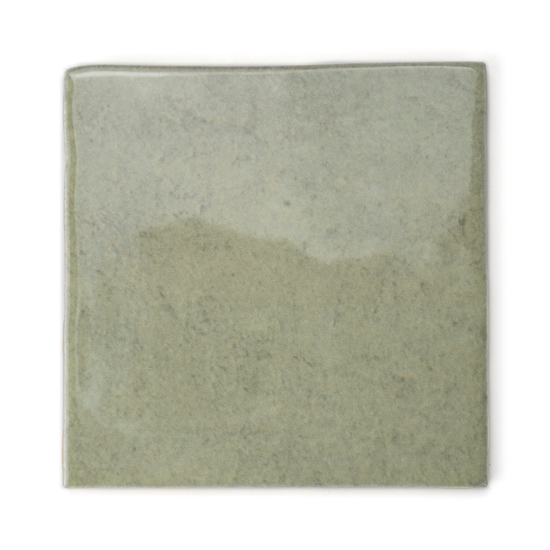 Un azulejo cuadrado verde brillante y apagado se asienta solo sobre un fondo blanco, mostrando una sutil textura de mármol con t