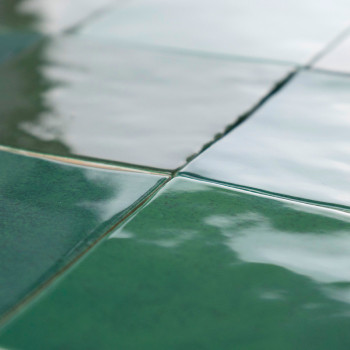 Los azulejos de cerámica verde forman un patrón de cuadrícula que refleja la luz con un acabado brillante y crea una superficie 
