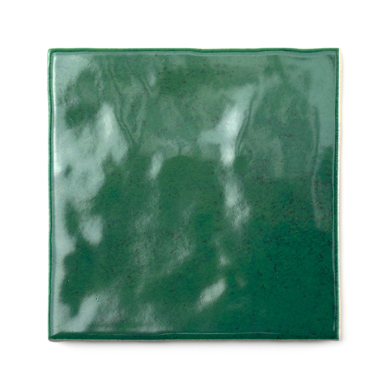Un carreau de céramique carré vert émeraude brillant avec une texture légèrement inégale réfléchissant la lumière, placé sur un 