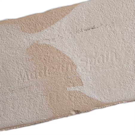 Un azulejo rectangular de color beige texturizado con manchas blancas irregulares. En la superficie aparece sutilmente grabado e