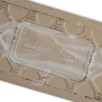 El azulejo cerámico beige presenta un patrón geométrico en relieve. Entre la textura se ve el texto en relieve `Made in Spain`.