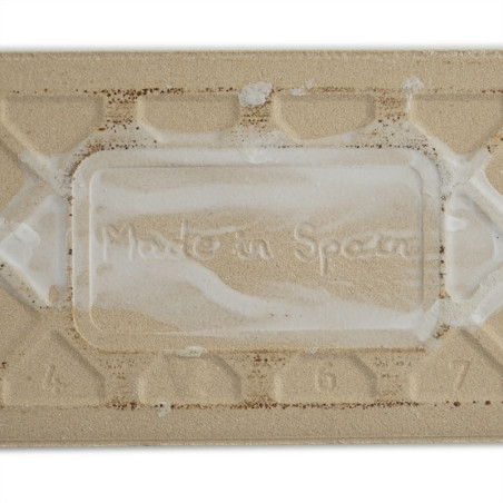 Een rechthoekige beige tegel heeft de opdruk `Made in Spain` in het midden, omgeven door verhoogde geometrische patronen en cijf