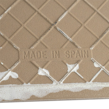 Die Fliese weist eine beige, rautenförmige Oberfläche mit leichten weißen Flecken auf. In der Mitte ist der Text „MADE IN SPAIN“