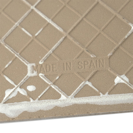 Een beige keramische tegel met een rasterpatroon met witte resten en de tekst `MADE IN SPAIN` in reliëfstijl.