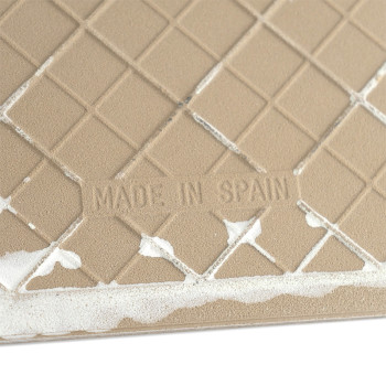Um ladrilho bege apresenta um padrão de diamante e o texto `MADE IN SPAIN` gravado nele. Resíduos de adesivo branco aparecem nas