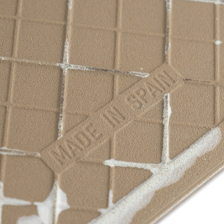 Um azulejo marrom texturizado, com a inscrição "MADE IN SPAIN" em relevo, exibe um padrão de grade. É parcialmente coberto com a