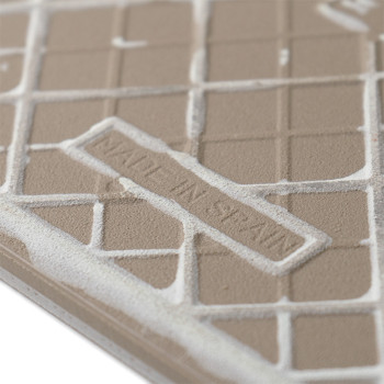 Un azulejo beige presenta patrones en relieve en forma de cuadrícula. El texto en relieve dice `MADE IN SPAIN`. La superficie de