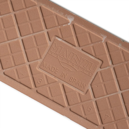 Un azulejo marrón rectangular con un patrón de cuadrícula en relieve. Presenta un logo central: `MAINZU` y `MADE IN SPAIN`, colo