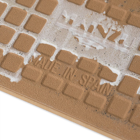 Die braune Fliese weist ein Raster aus quadratischen Vertiefungen auf. Der abgenutzte weiße Text lautet „MADE IN SPAIN“, mit tei