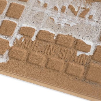 Um ladrilho cerâmico texturizado apresenta um padrão de grade com quadrados ligeiramente elevados. O texto `MADE IN SPAIN` está 